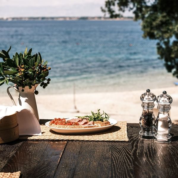 A meal on a table with a seaside view, featuring pizza, salt and pepper shakers at Falkensteiner Hotels & Residences