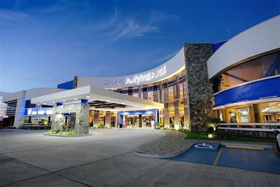 A wide-angle exterior view of the Hotel Mykonos entrance at dusk with lit signage and stonework