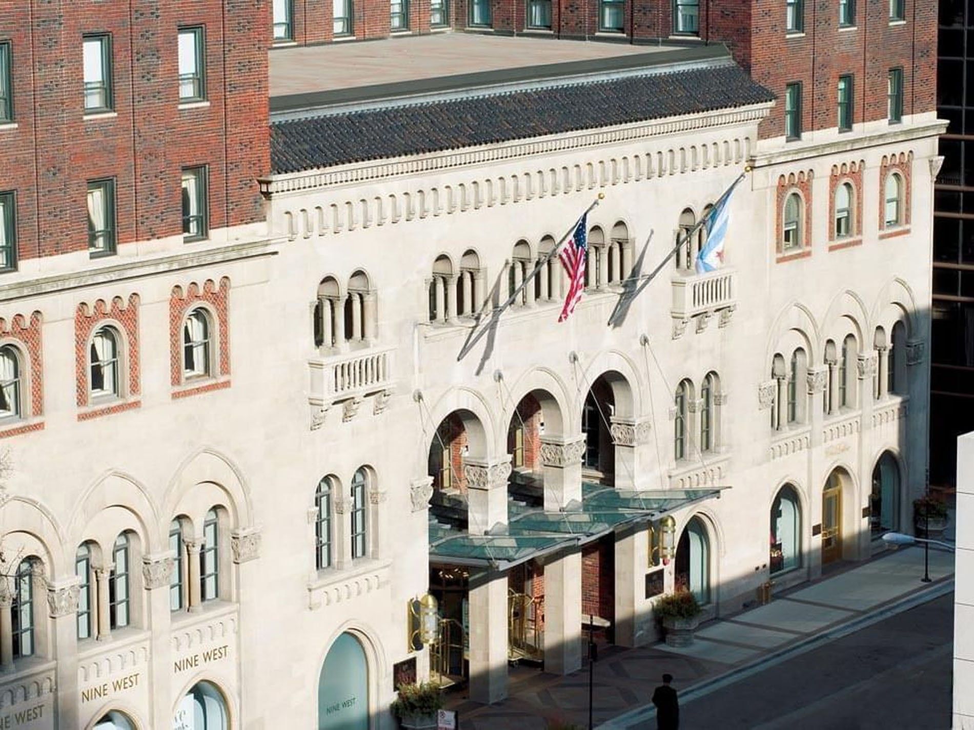 An elegant facade with arched windows, two flags, and a canopy entrance at Warwick Allerton Chicago.