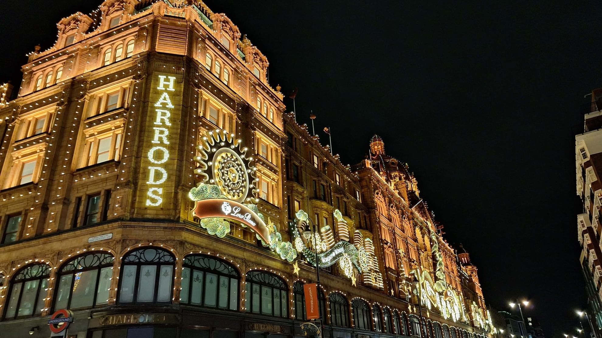 Illuminated Harrods building at night with decorative lights and vehicles on the street.