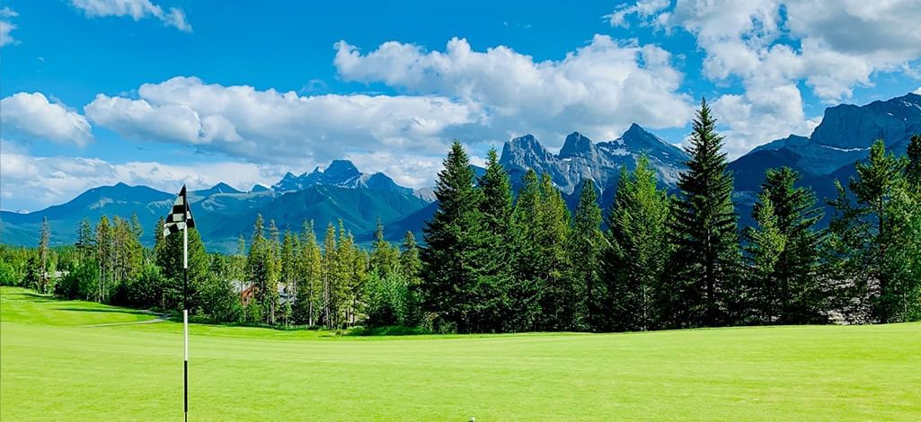 A Canmore golf course on a sunny day with the mountains in the backdrop.