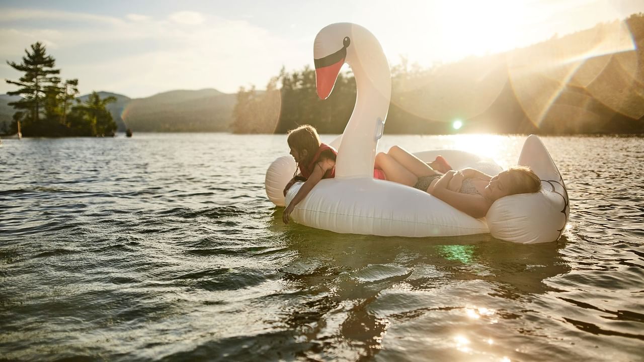 Two children relaxing on a large inflatable swan floating on the Penticton River near Coast Penticton Hotel