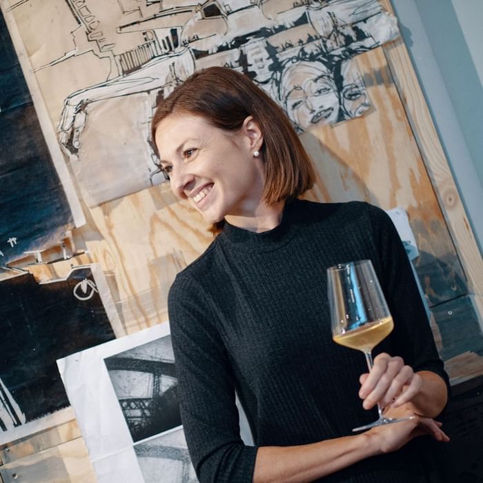 Jasmin Jaunegg vintner in a black sweater, holds a glass of white wine at Hotel Motto Vienna