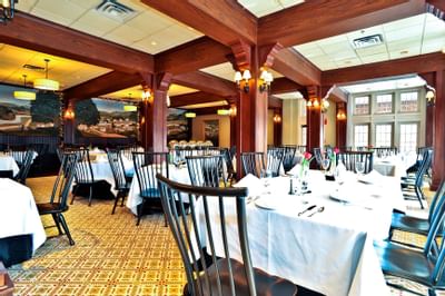 Spacious dining room featuring white tablecloths on tables set with black wooden chairs and beams at The Simsbury Inn