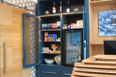 Snack cabinet, featuring blue storage shelves full of items and a mini-fridge under LED lights at Hotel Keen
