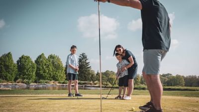 A family is playing golf on a sunny day, with a flag in the background.