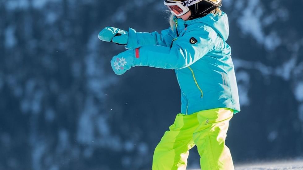 A kid in ski wear playing with snow near Falkensteiner Club Funimation Katschberg