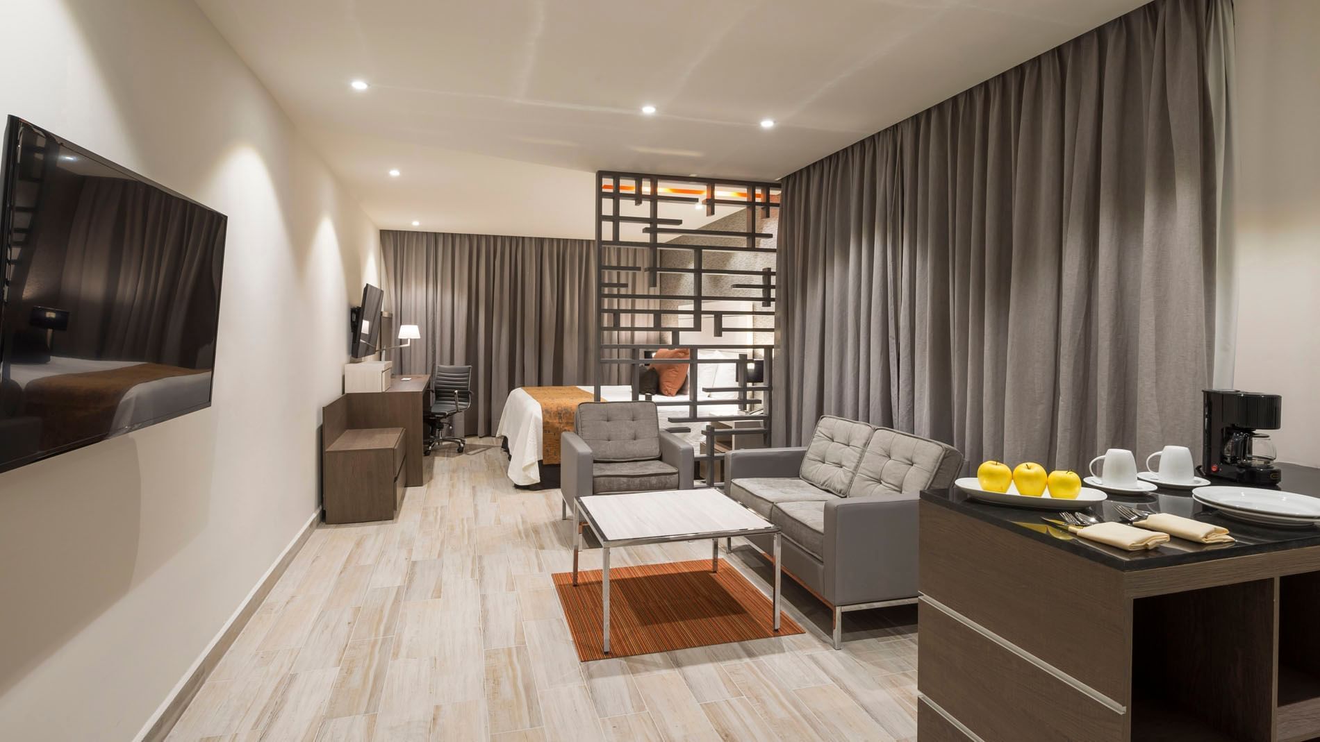 King Long Stay Suite living area featuring a grey sofa, a geometric divider, and a cozy bedroom nook at Real Inn Celaya