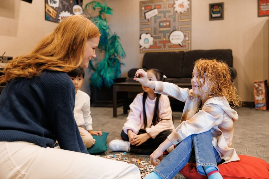 Adult woman and three children sitting on cushions on the floor playing with puzzle pieces at the Rodd Royalty hotel
