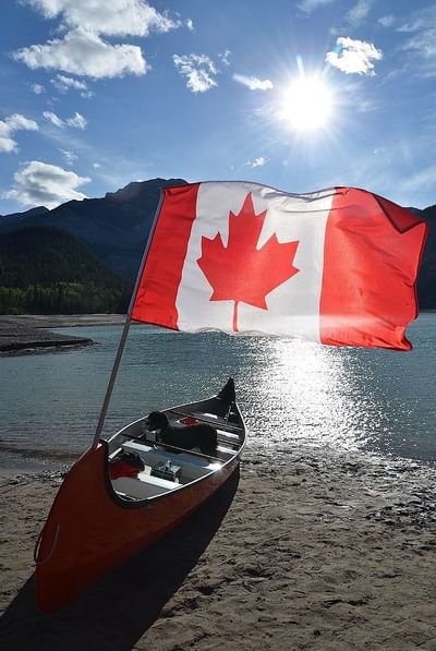 Vibrant Canadian flag waving beside an orange canoe on a sandy shore near Blackstone Mountain Lodge