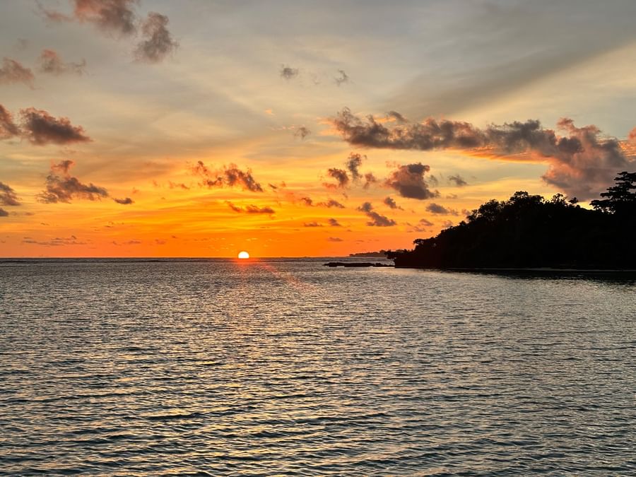 Sunset over ocean with silhouetted trees and clouds at Warwick Le Lagon Vanuatu.