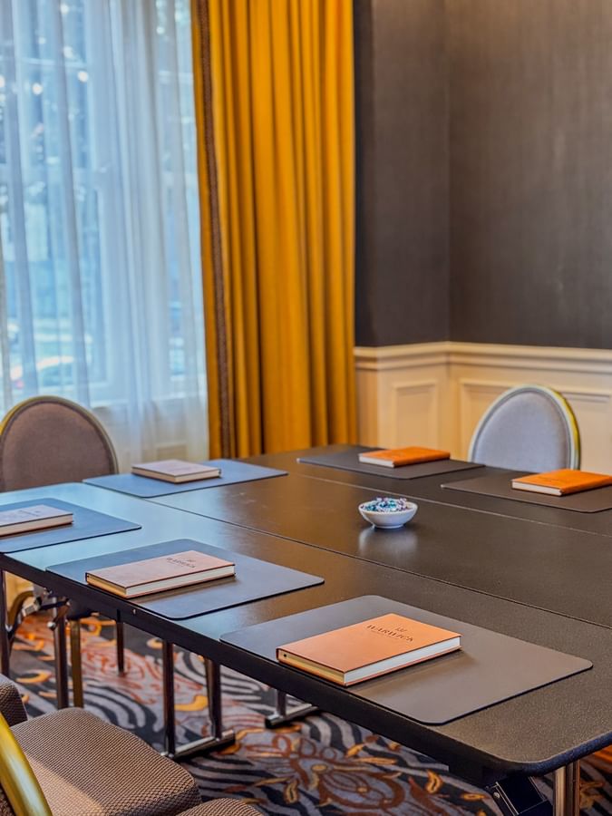 Boardroom with Brown notepads on a black table by yellow drapes at Warwick Melrose Dallas