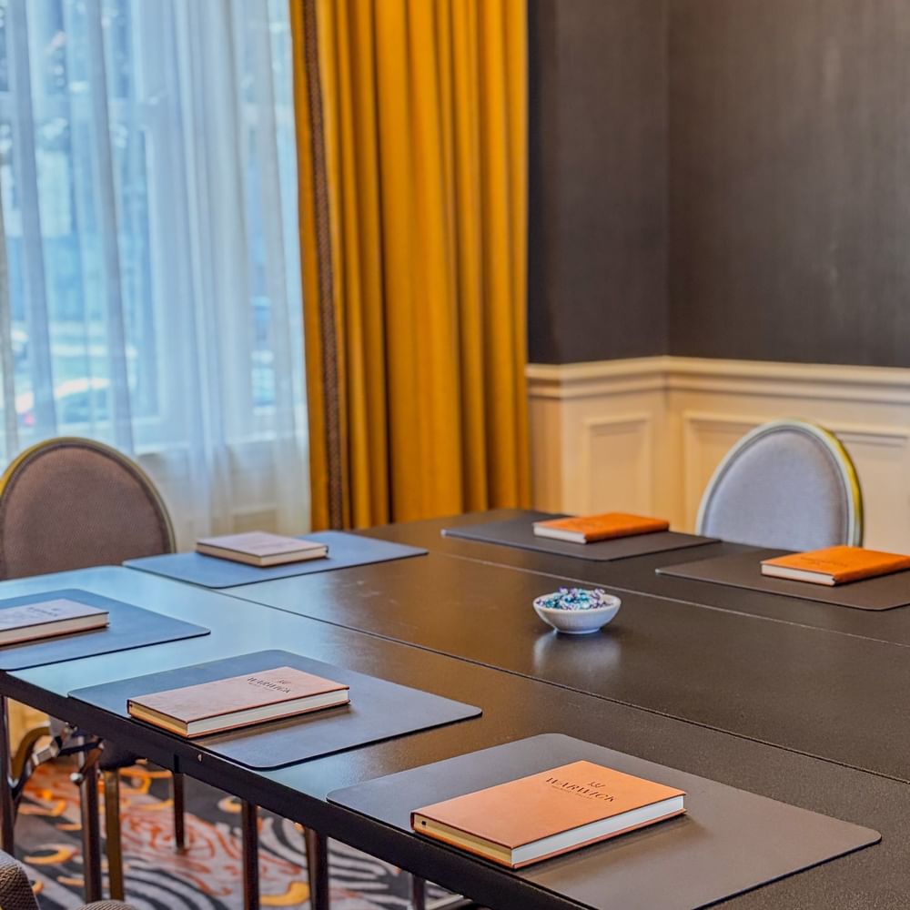 Boardroom with Brown notepads on a black table by yellow drapes at Warwick Melrose Dallas