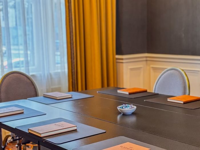Boardroom with Brown notepads on a black table by yellow drapes at Warwick Melrose Dallas