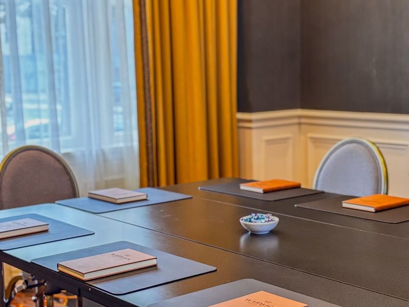 Boardroom with Brown notepads on a black table by yellow drapes at Warwick Melrose Dallas