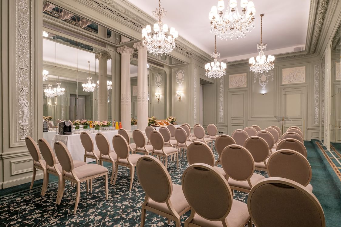 Salle de réception élégante avec lustres en cristal, moulures ornementales et chaises roses disposées en rangées à Hotel Westminster Warwick Paris