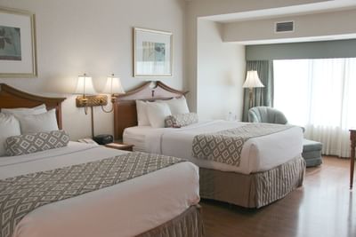 Two Queen Beds - ADA featuring beds between lamps with wall art beside window lounge chair at Clayton Plaza Hotel