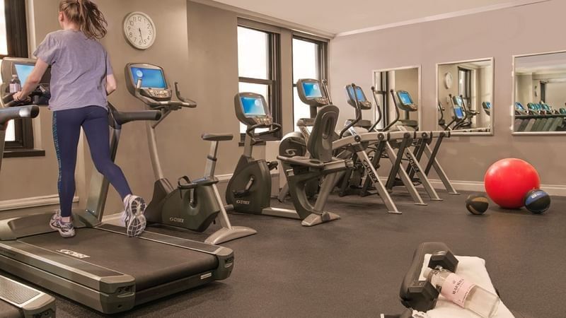 Woman running on a treadmill in a hotel fitness center with workout machines at Warwick New York