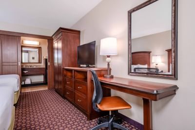 Guest room with mirror, wooden desk, chair, TV, dresser, and bathroom vanity at Rosen Inn International