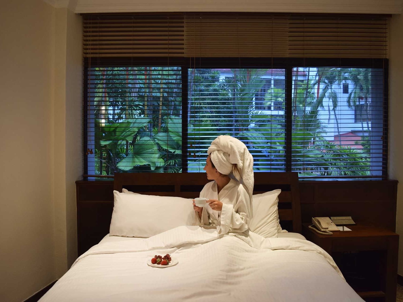 A lady in bathrobe having a tea in bed at York Hotel Singapore