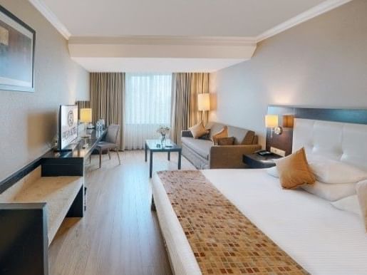 A hotel room with a large bed, couch, desk, and chair, featuring modern decor and furnishings.