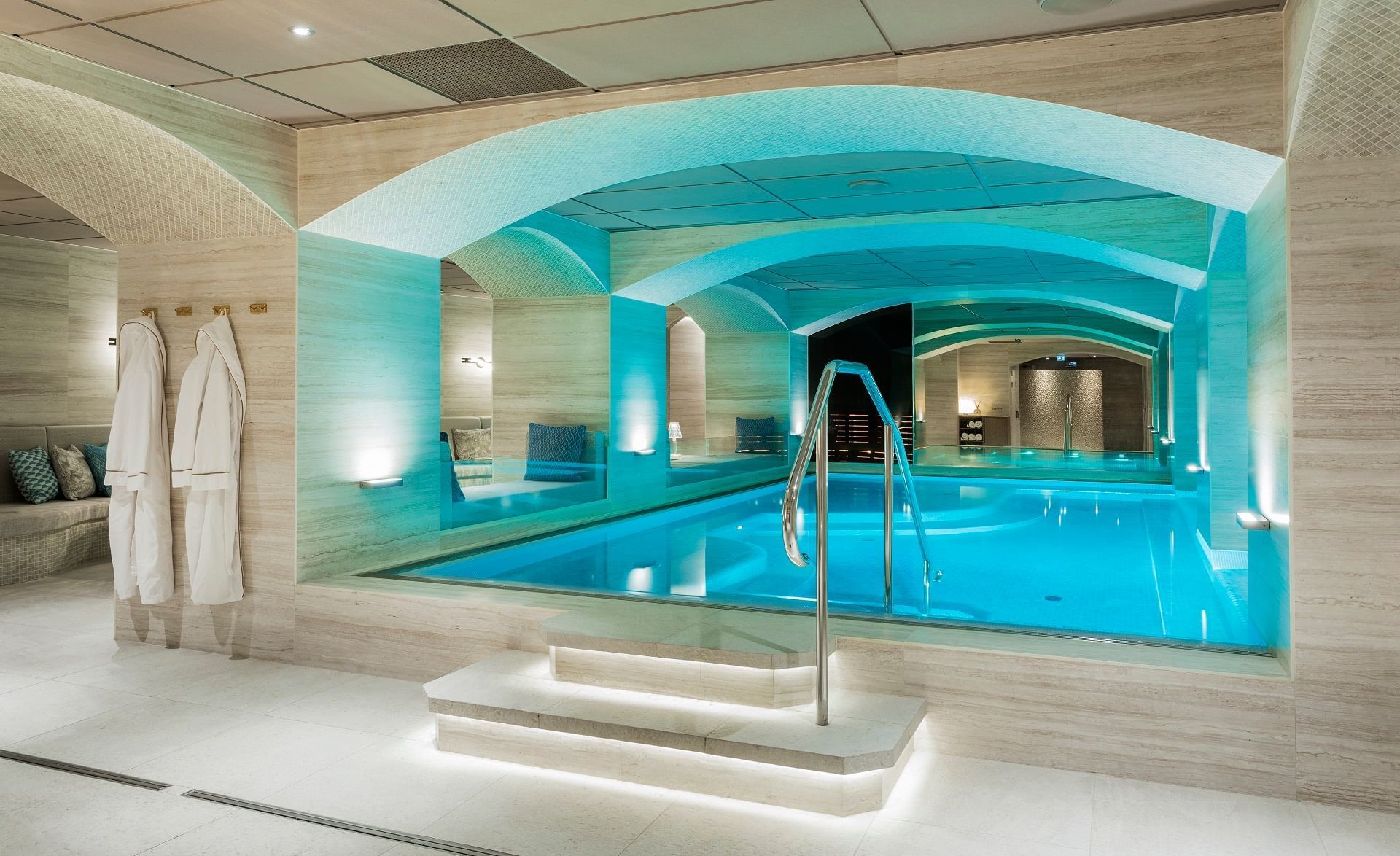 Indoor pool with blue lighting, handrails, and white robes hanging on the side.