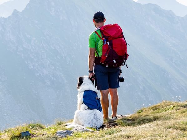 Man with backpack and dog on mountain trail.