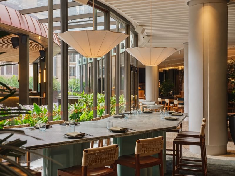 Elegant dining area with large table and modern chairs under decorative lamps for The Suite Life offer.
