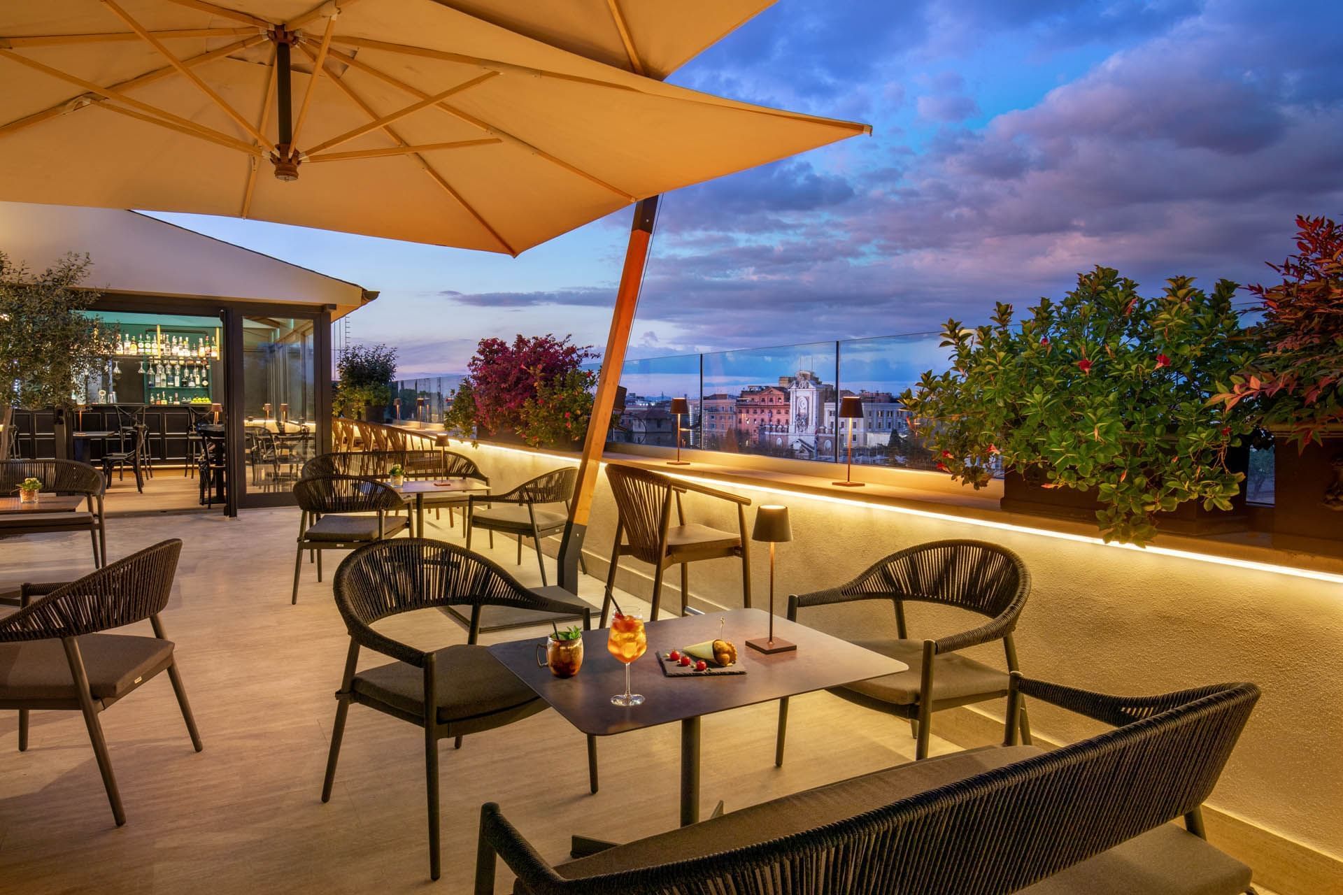 Terrazza Costanza rooftop at The Guardian Hotel with modern seating, and a twilight city view