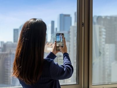 Woman taking a photo of the cityscape from her window at UniLodge Brisbane City.