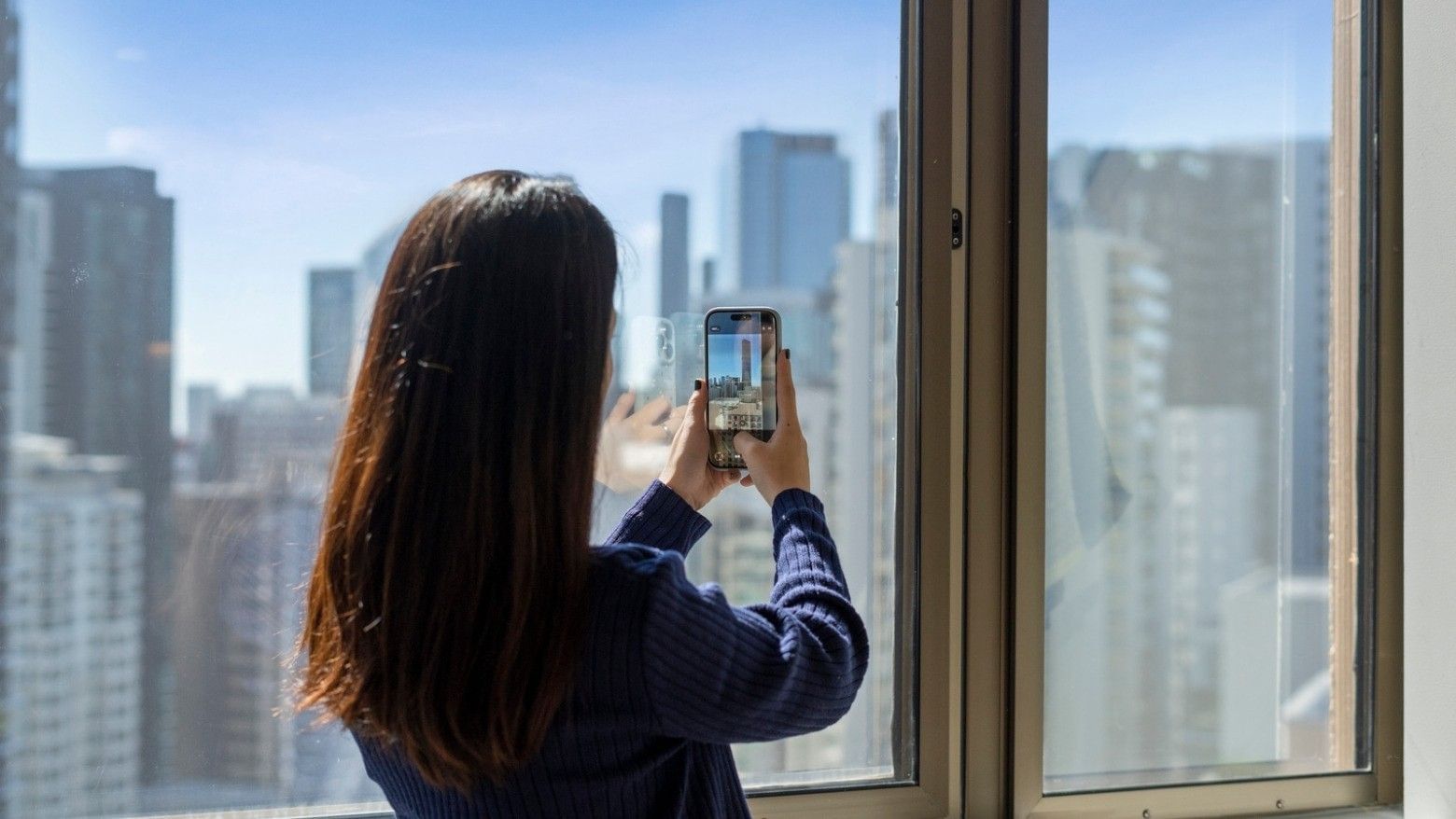 Woman taking a photo of the cityscape from her window at UniLodge Brisbane City.