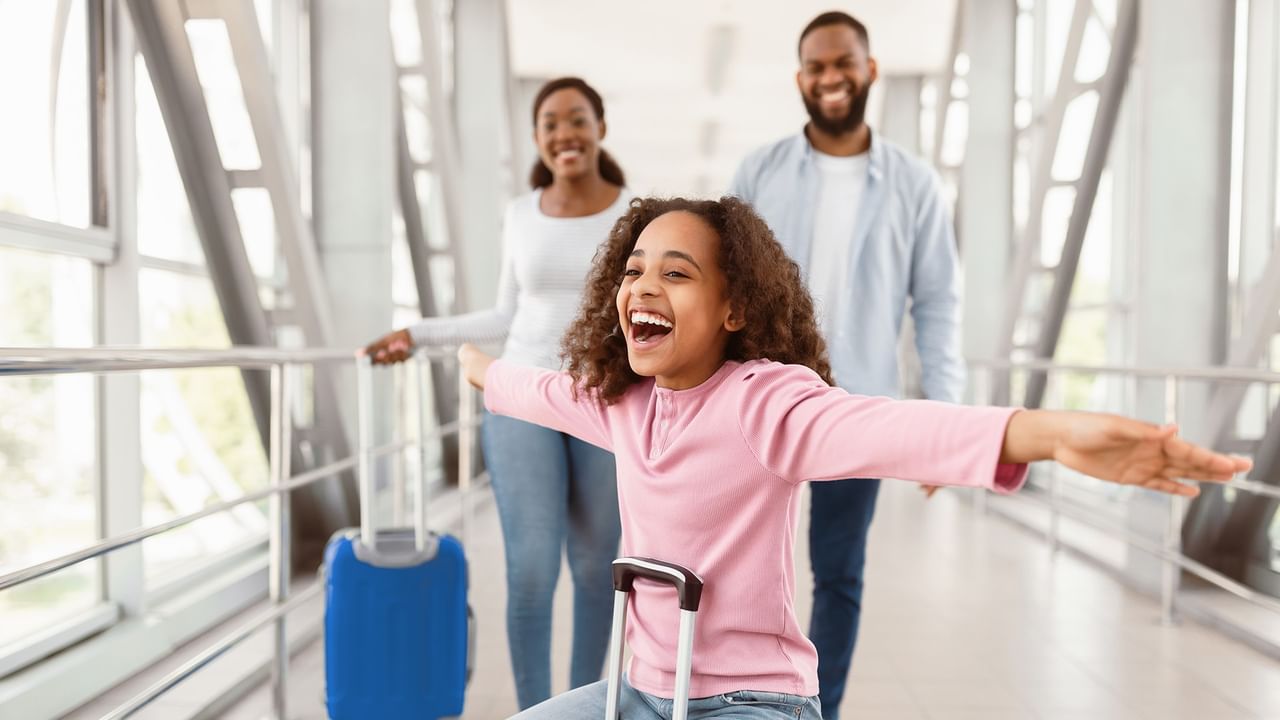 Excited girl with open arms in an airport with a smiling family and luggage.