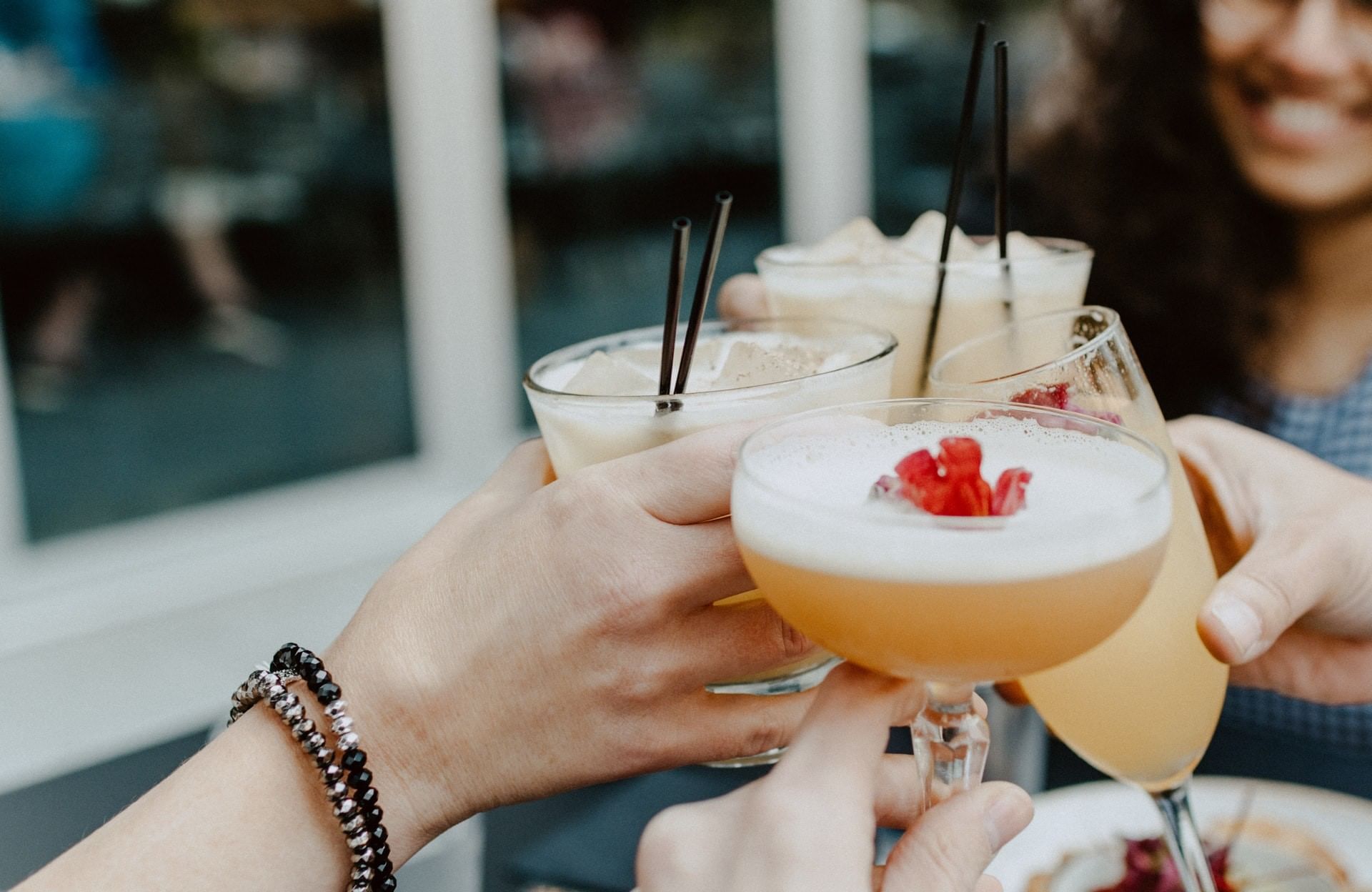 A close-up of hands holding and toasting cocktail glasses with straws.