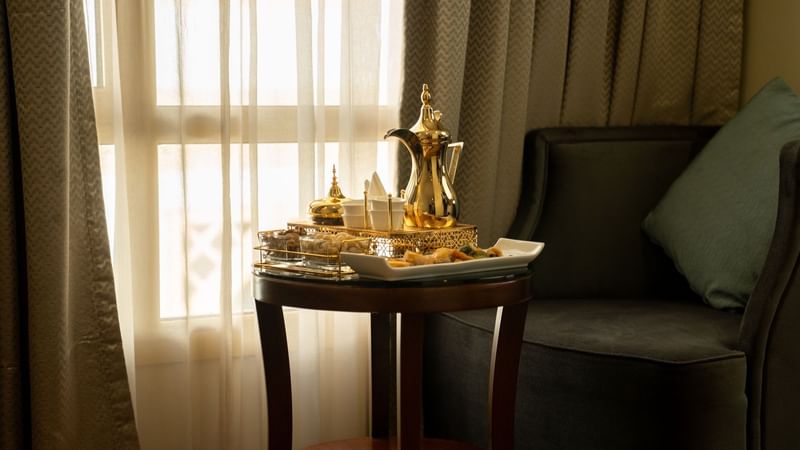 Coffee table with a tray and a teapot near an armchair in the Executive King Room at Saja by Warwick Madinah.
