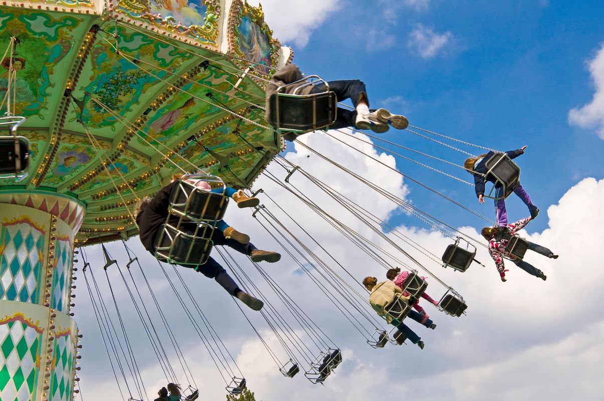 Carousel swings by riders under a blue sky, surrounding a vintage pillar near Warwick Paris Champs Elysées