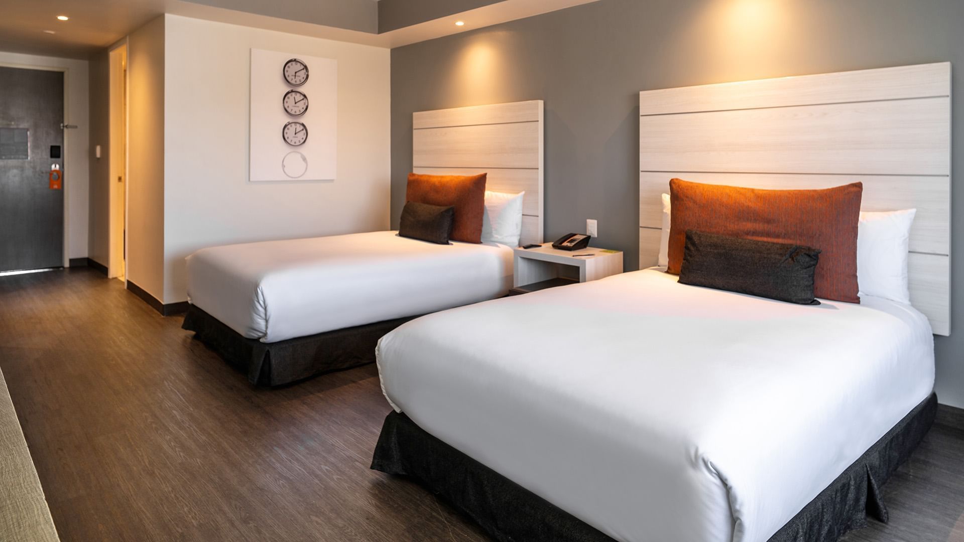Wall clock display and nightstand by the cozy beds in the Two Double Executive Room with wooden floors at Real Inn Tijuana