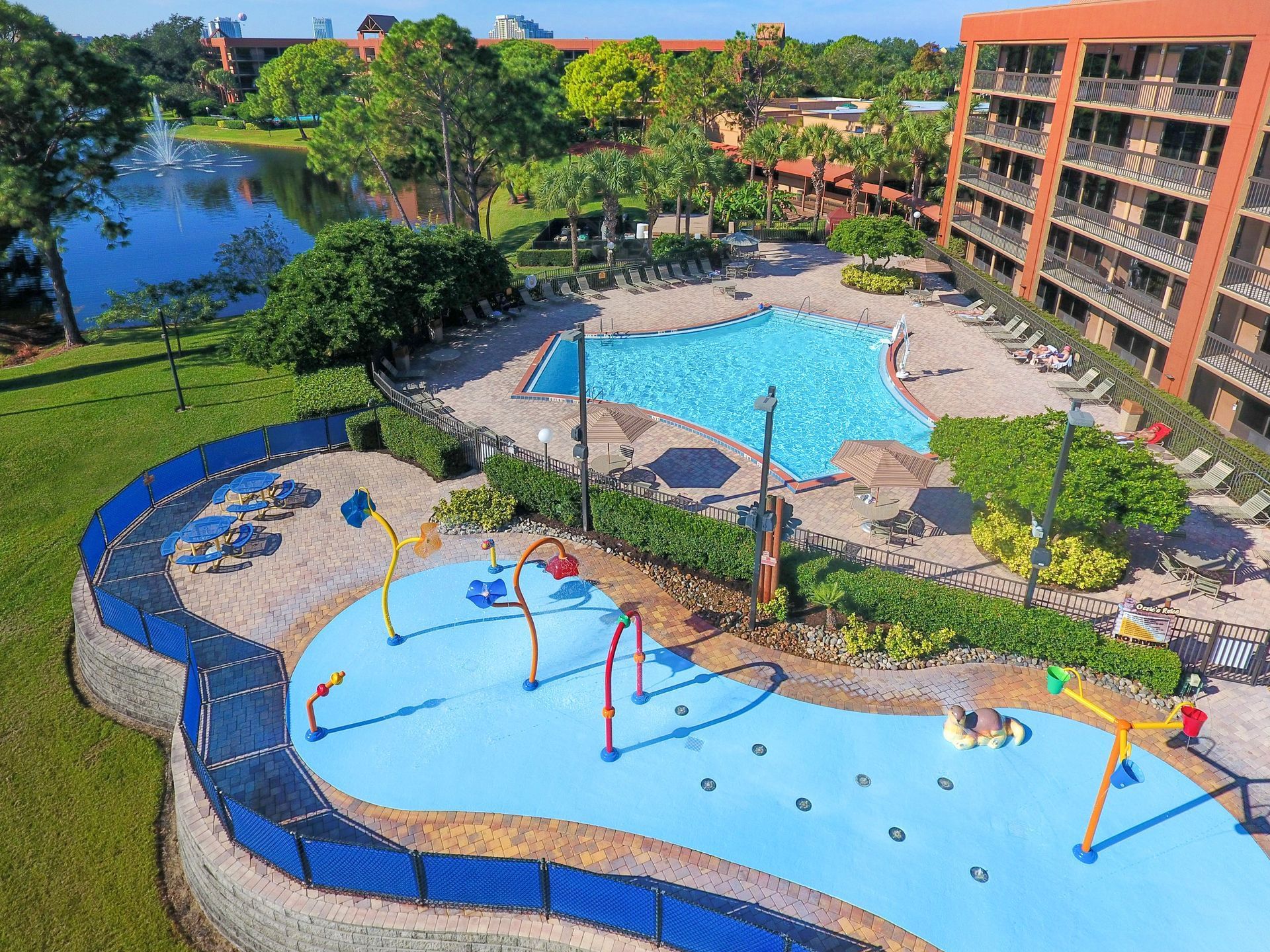 A colorful splash pad beside a pool and a large hotel building. 