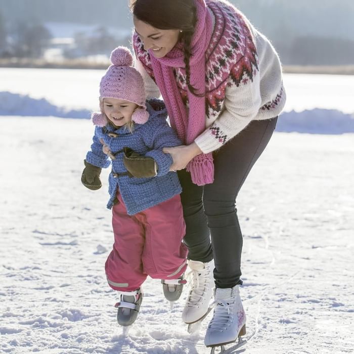 Mother helping her kid to ice-skating near Falkensteiner Hotels