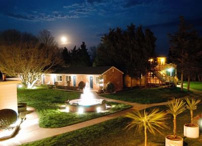 Nighttime view of a boutique motel with a lit fountain, surrounded by greenery at Breezeway Boutique Hotel