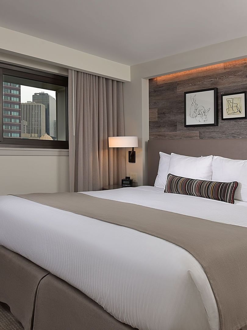 King bed by a window under framed art on a wood-paneled wall in Classic Rooms at Warwick Denver