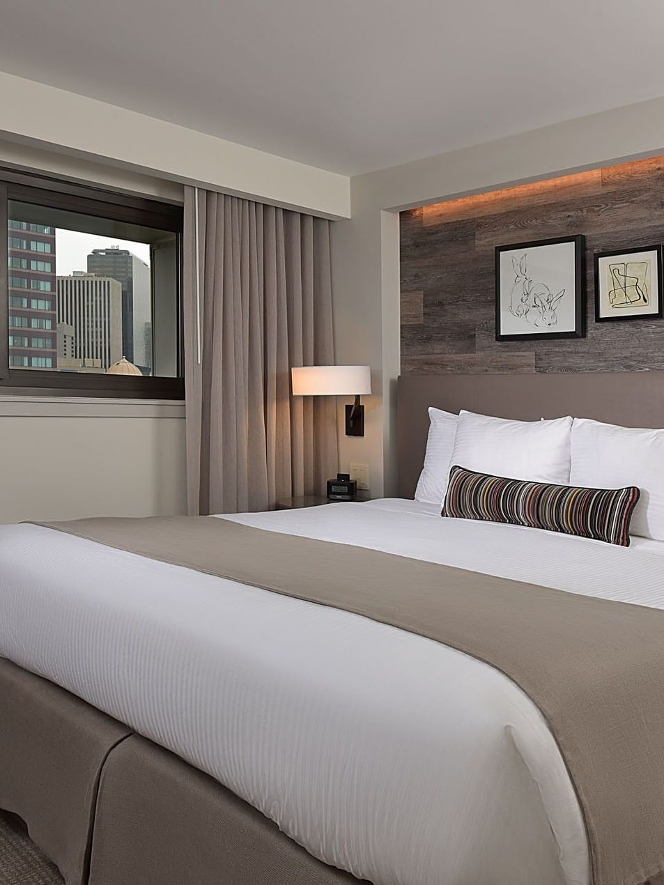 King bed by a window under framed art on a wood-paneled wall in Classic Rooms at Warwick Denver