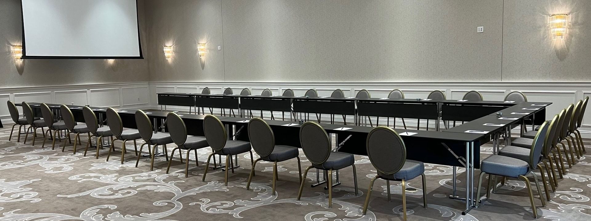 Meeting chairs by U-shaped tables under a projector screen in Turtle Creek Ballroom C at Warwick Melrose Dallas