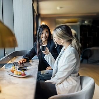 two women in a meeting, one is having coffee while the other smiles 