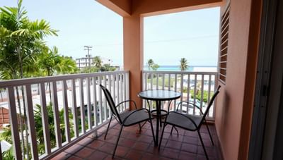 Two dark chairs and a small round table on a tiled balcony with a scenic ocean view at Worthing Court Apartment