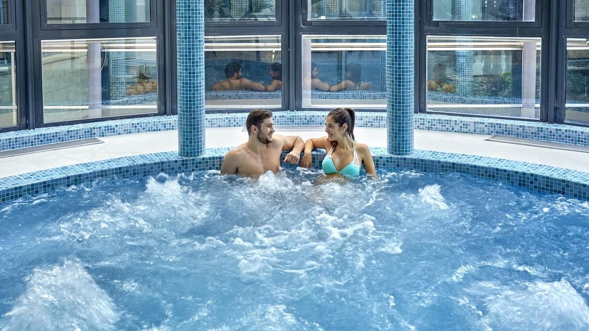 Couple en maillot de bain dans un jacuzzi intérieur avec des fenêtres.