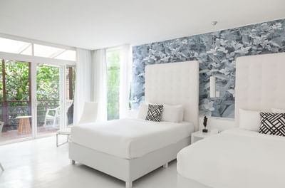 Bright Deluxe Room - 2 Queen Beds with modern furniture and a balcony overlooking lush greenery at Le Cameleon Hotel