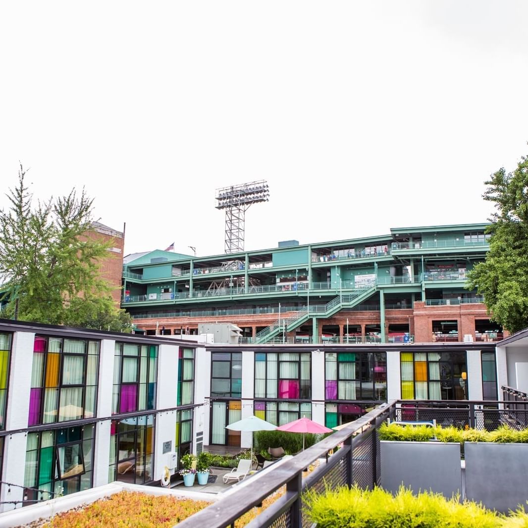 Modern boutique hotel with colorful window panels and rooftop garden overlooking Fenway Park's iconic green stadium structure