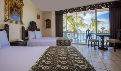 Spacious hotel room with two beds, decorative runners, and balcony overlooking palm trees at Playa Los Arcos Puerto Vallarta