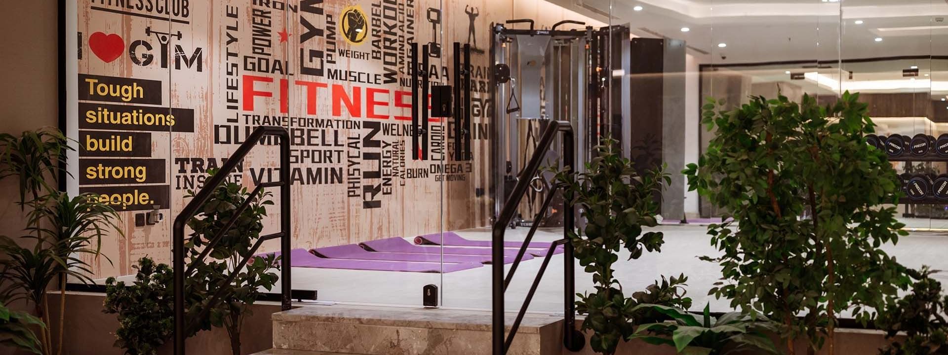 Marble stairs by green plants leading to a gym with yoga mats under a typographic wall at Cantonal Hotel by Warwick Riyadh
