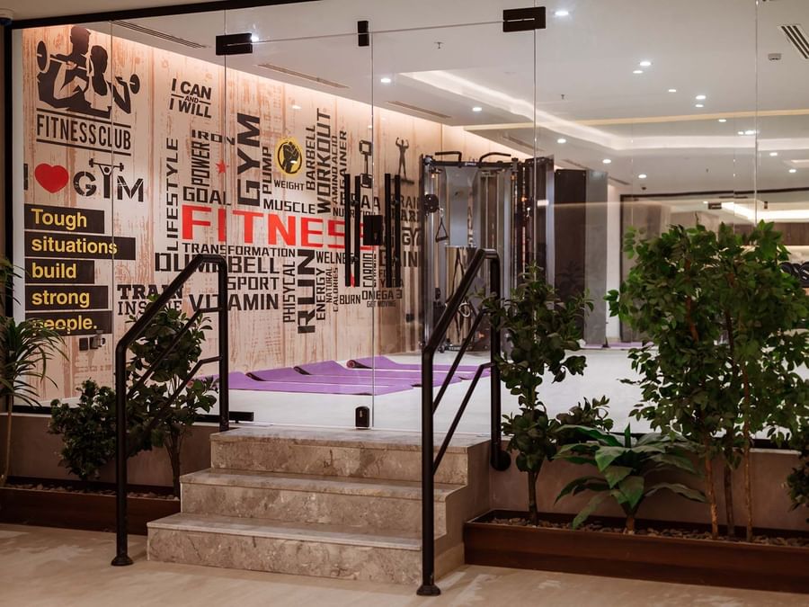 Marble stairs by green plants leading to a gym with yoga mats under a typographic wall at Cantonal Hotel by Warwick Riyadh